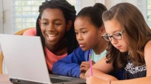 Three students gather around a laptop to study together