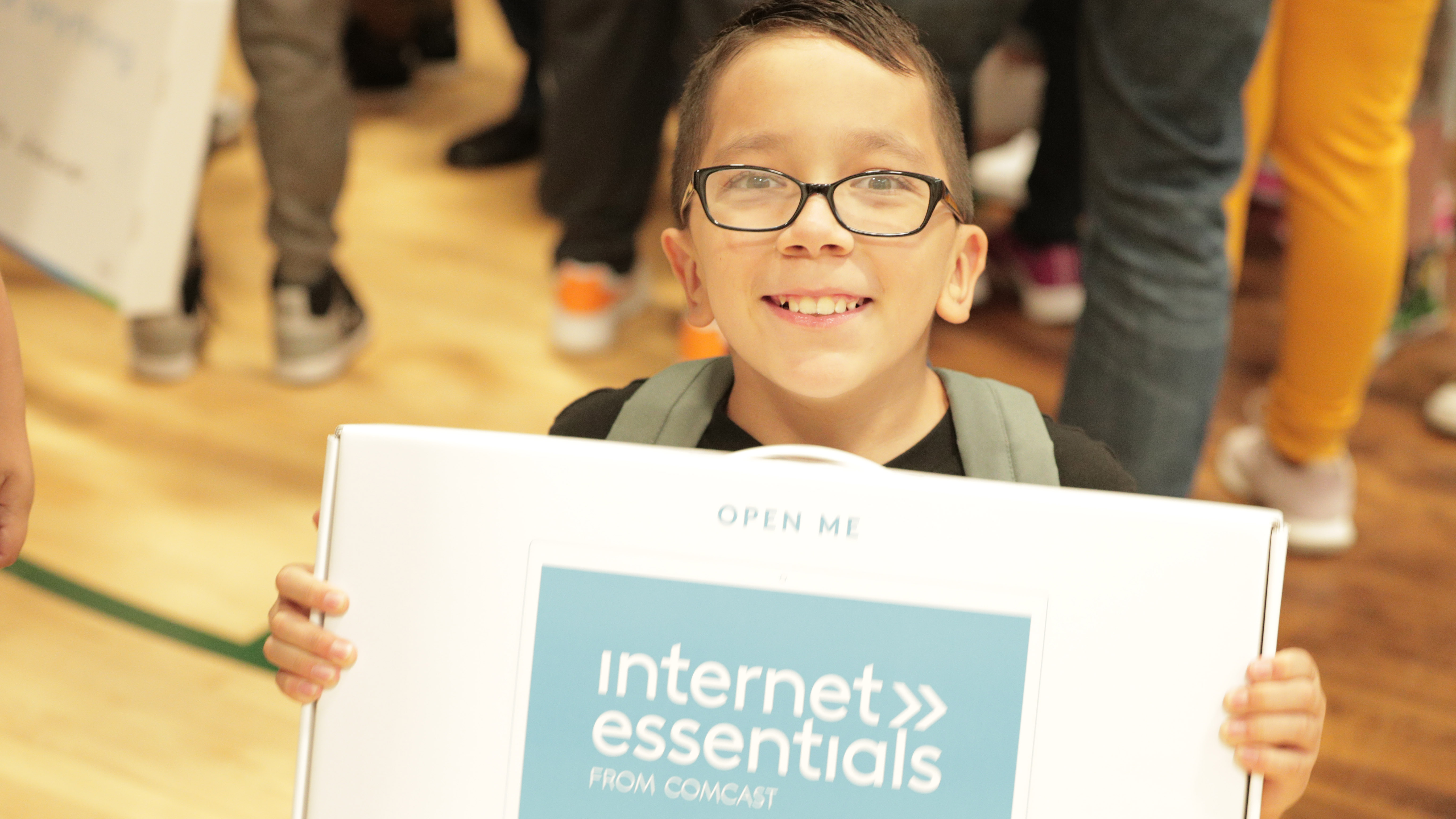 A child holds up their new Internet Essentials laptop at an event in Denver.