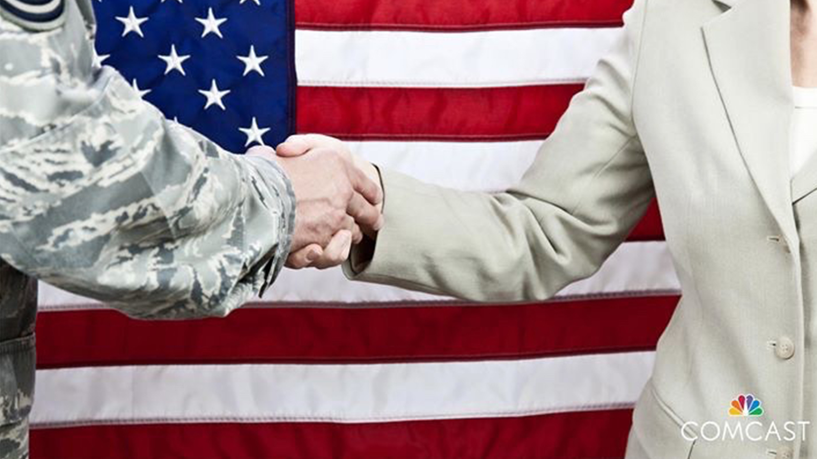Two people shake hands in front of an American flag.
