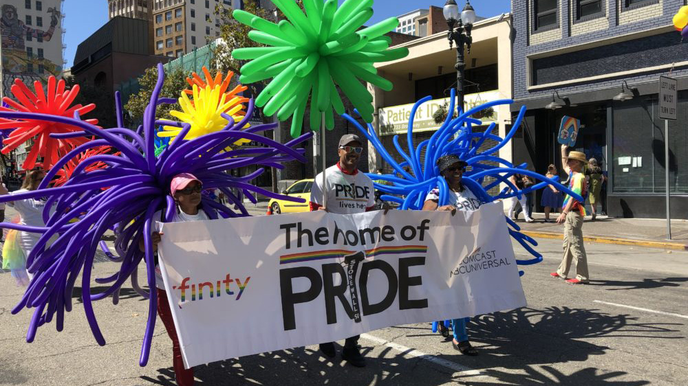Comcast employees hold a Pride banner as they march in a parade.