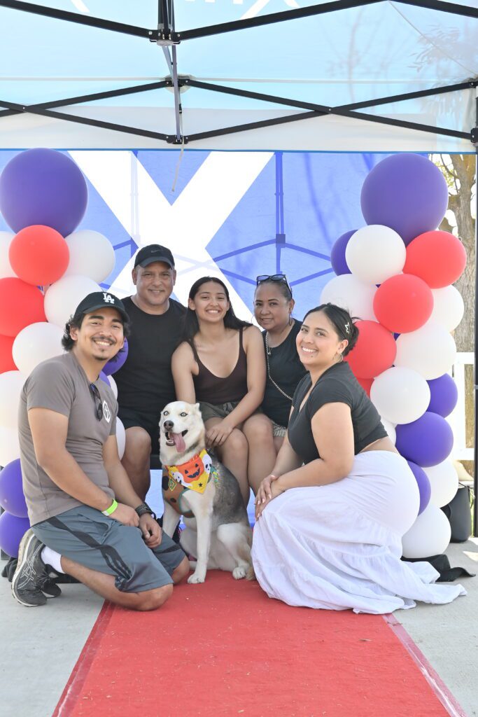 A family of five and their dog wearing a bandana sit and pose for a photo on the red carpet at Xfinity's booth at Tesoro Viejo in Madera