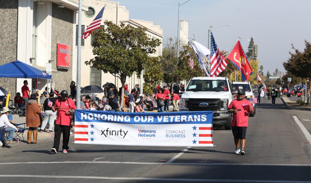 Xfinity trucks and Comcast teammates walk and hold a banner that reads, "Honoring our veterans," in the Central Valley Veterans Day Parade 2023.