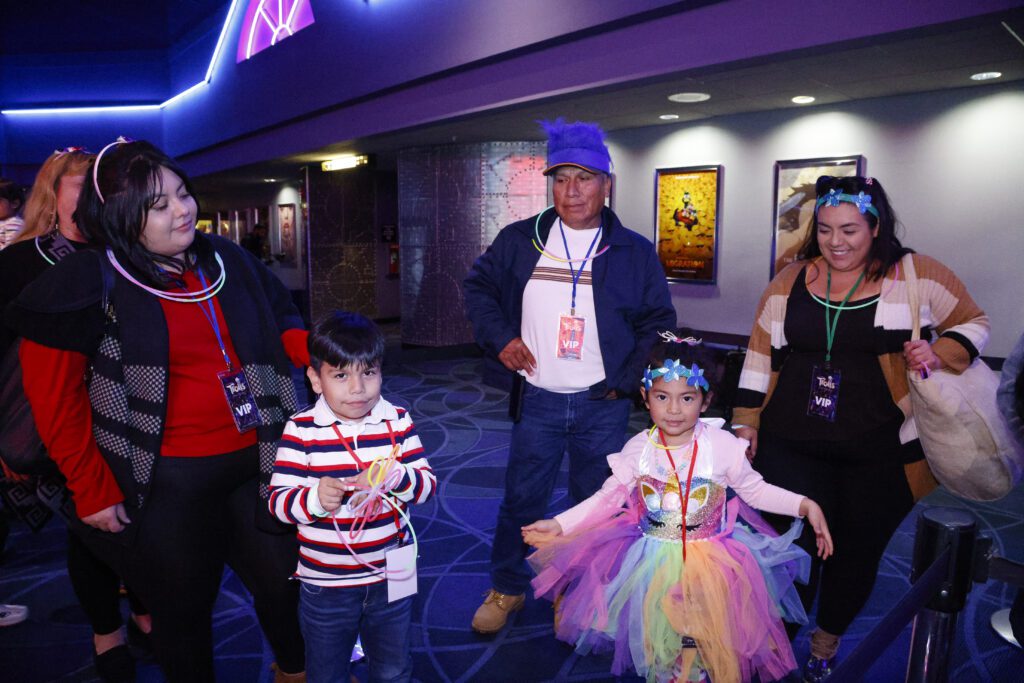 A family smiles as they stand in live to see the new Trolls Band Together movie