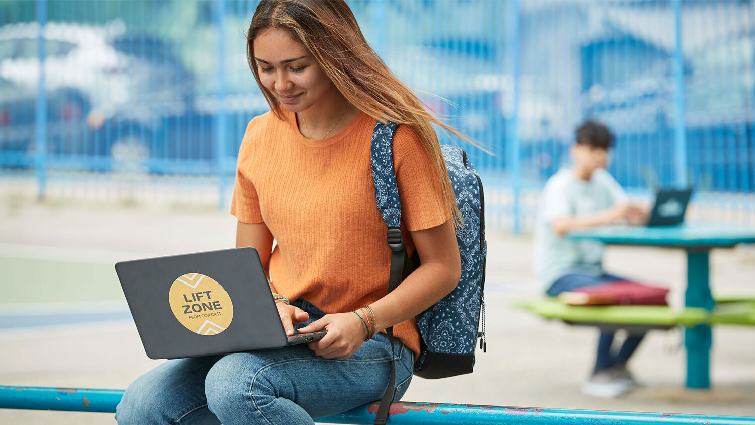 A young woman types on a laptop outdoors.