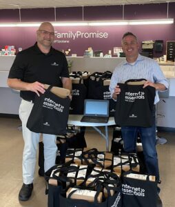 Representatives from Comcast and Family Promise of Spokane smile with bags with laptops in them at a Family Promise office.