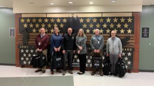 A Comcast representative and military community organization representatives pose with laptops in front of veteran mural.