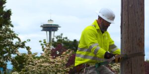 A Comcast technician works on a power pole with the Space Needle in the background.