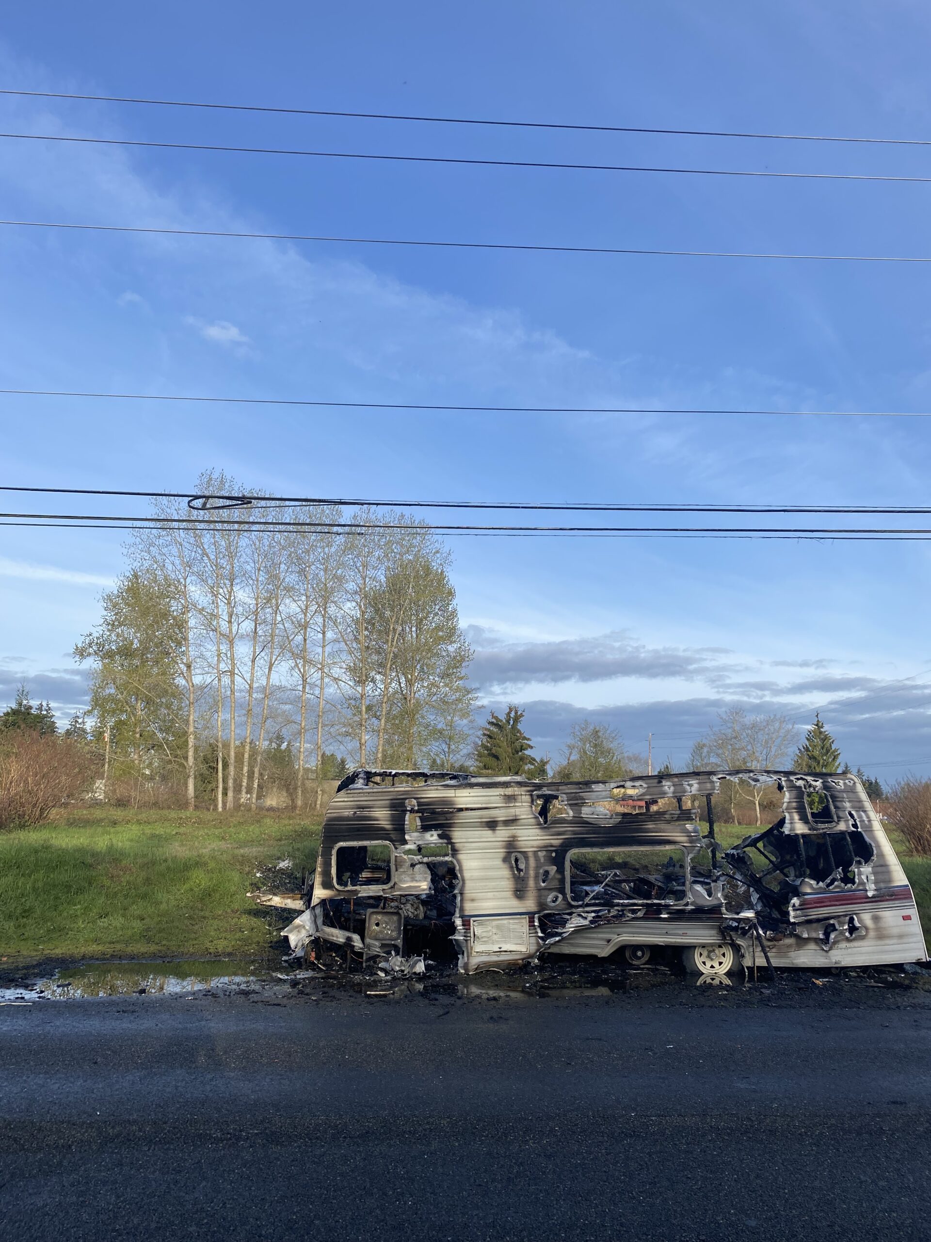 A burned camper trailer on the side of a road.