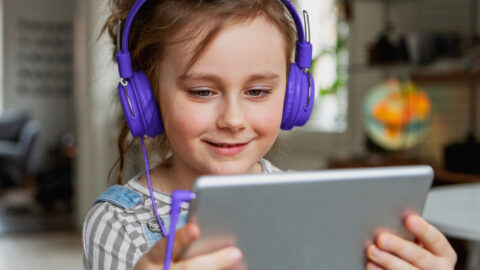 A young girl holds a tablet computer with headphones on.