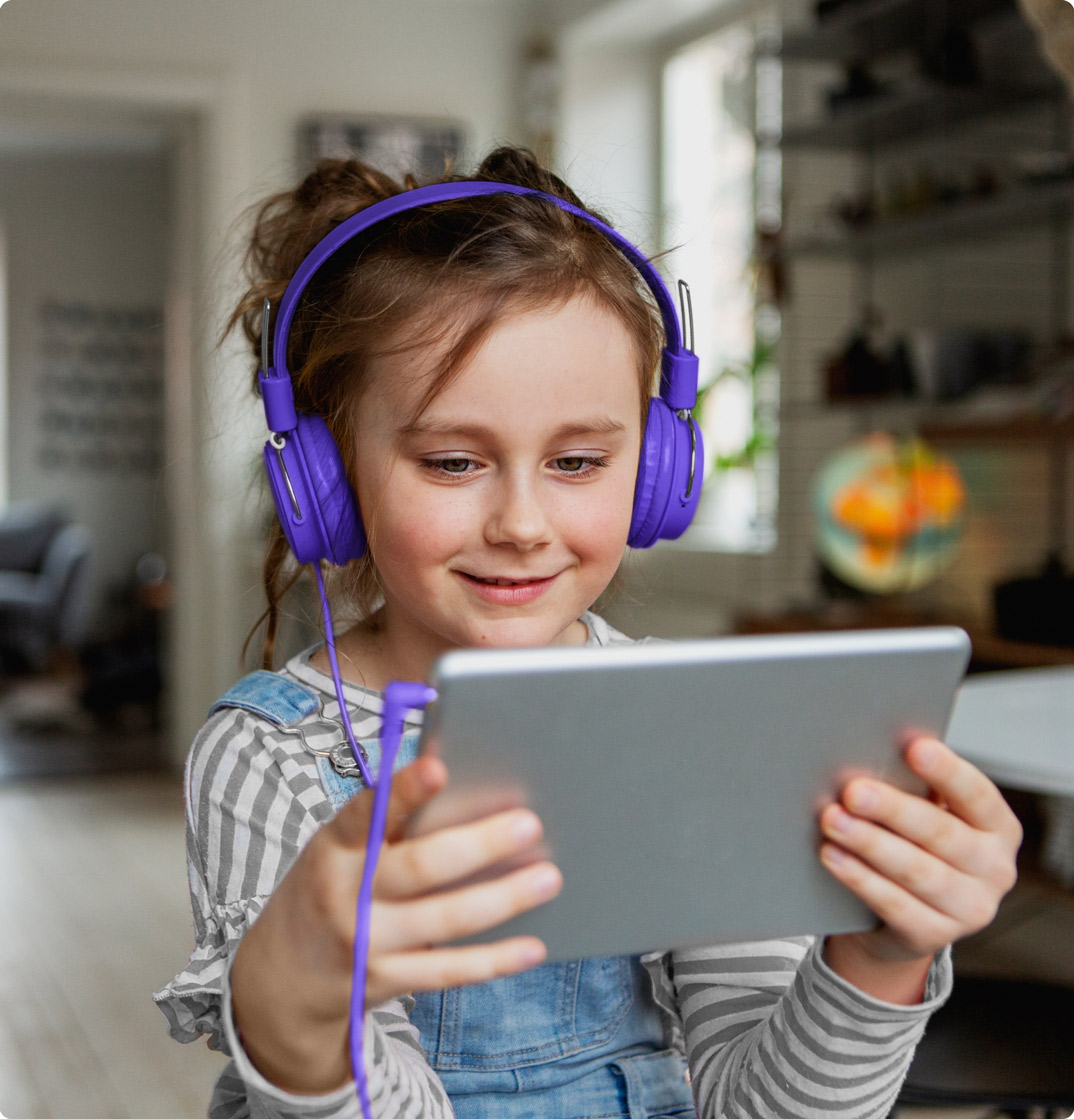 A young girl holds a tablet computer with headphones on.
