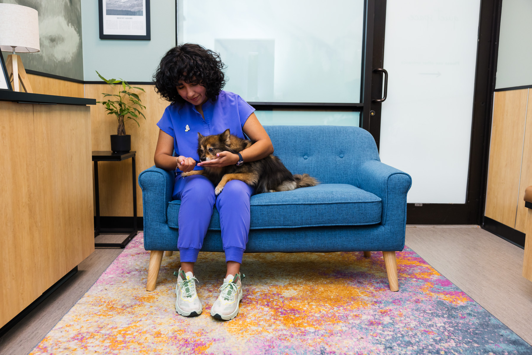 A Cara Veterinary employee sits with a dog on a couch.
