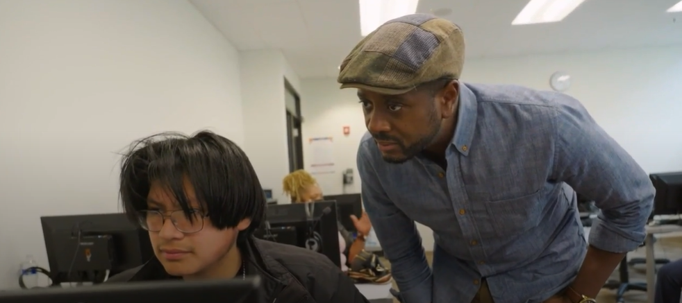 David Pierre-Louis works with a student at a computer in a classroom.
