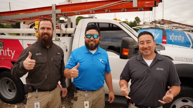 Three technicians standing next to an Xfinity truck smiling and posing for a picture