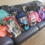 Many backpacks on a grey sofa