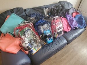 Many backpacks on a grey sofa