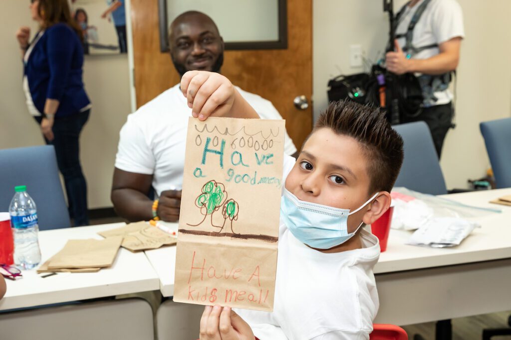 A young boy holding up paper bag with drawn picture and written note on it