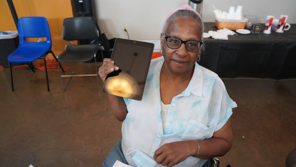 Older woman holding up a tablet.