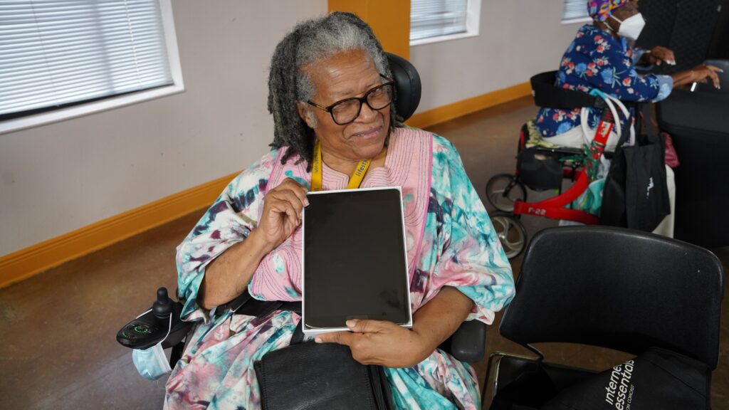 Older woman in wheelchair holding up tablet.
