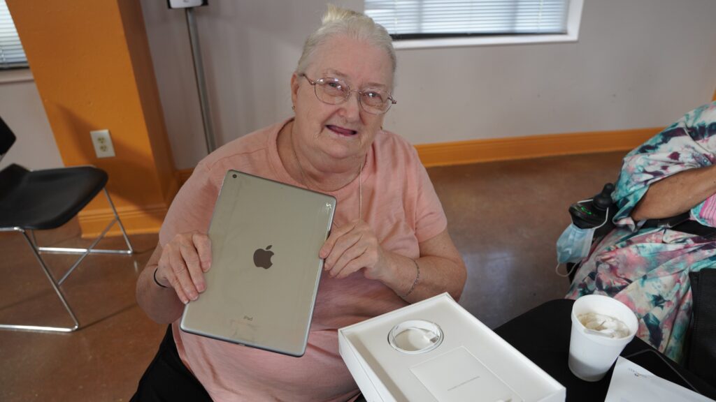 Older woman wearing glasses and pink shirt holding up iPad
