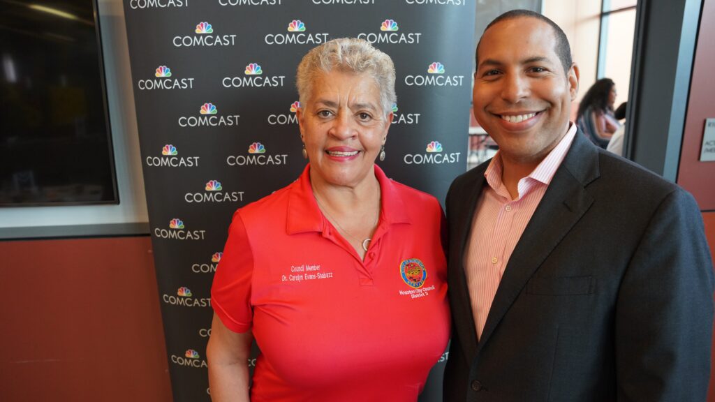 Two people smiling and posing for a picture in front of Comcast logo wall