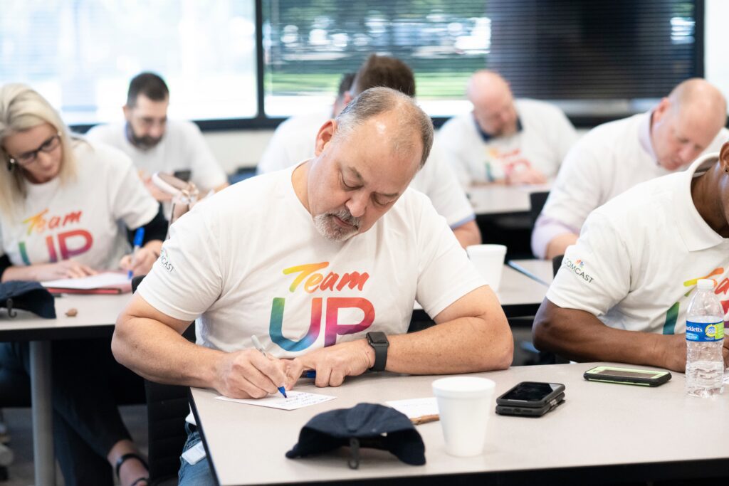 Multiple people wearing Team Up t-shirts sitting at tables and writing on notes