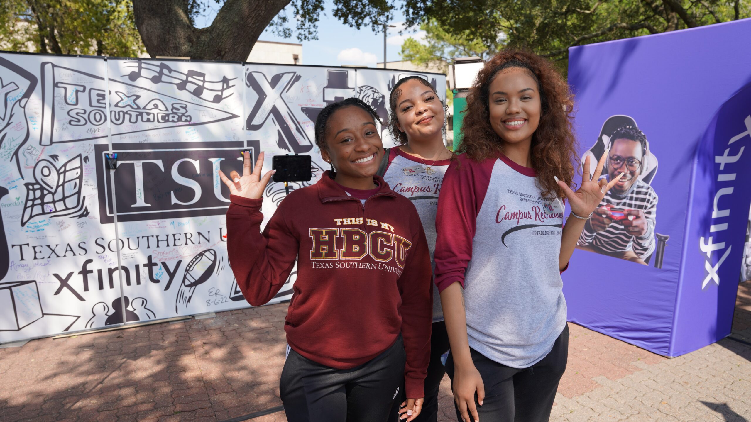 Three young women pose in front of TSU and Xfinity signs.
