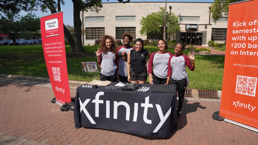 Five students posing with smiles behind a table at an Xfinity booth