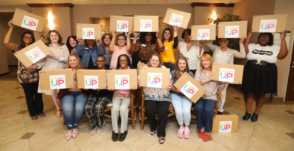 Multiple women posing for a picture together holding up laptop boxes with Project Up logos