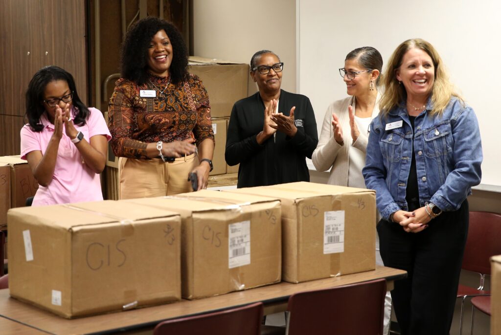 Five women standing behind a table that has three large cardboard boxes