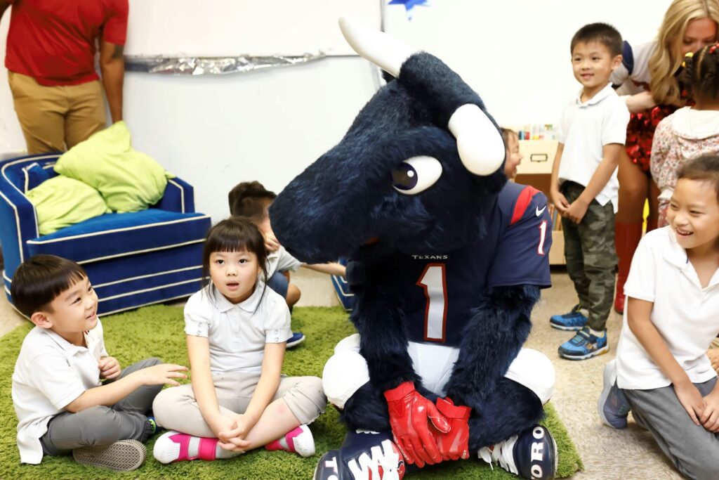 Mascot seated on green rug looking at two young children