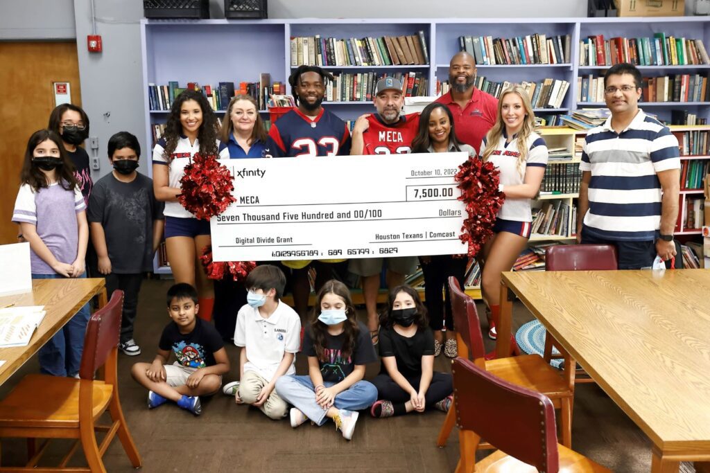 Volunteers and children posing together inside a library with a large check