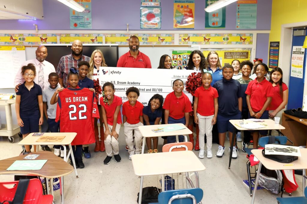 Group of volunteers and children posing for picture in classroom with large check