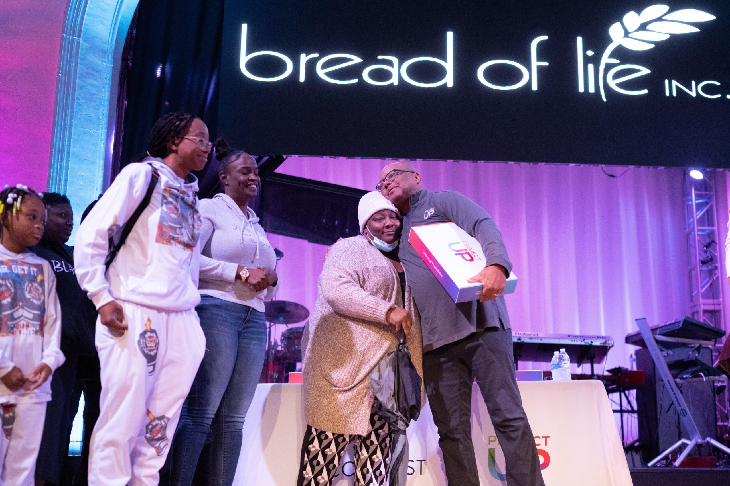 Comcast's Executive VP of Digital Equity and Executive VP of Public Policy Broderick Johnson is seen on stage, giving away a laptop to a woman.