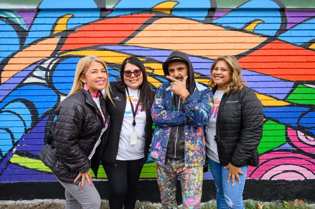 Three volunteers posing with the artist in front of the mural