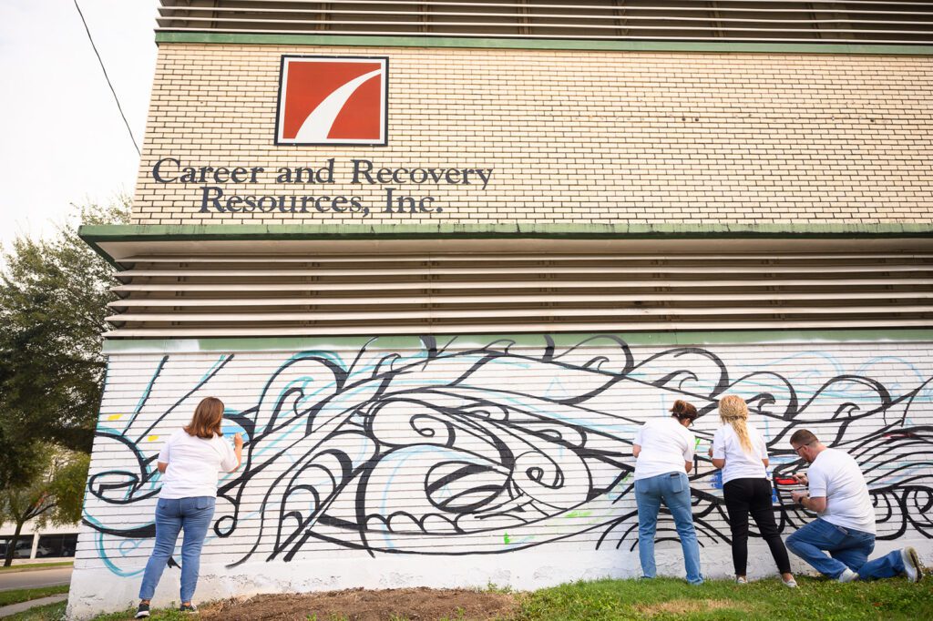 Four volunteers starting to paint on the mural on brick building