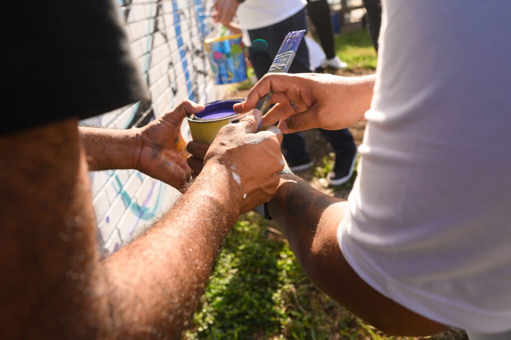 Close up on two volunteers hands holding a can of blue paint and brushes