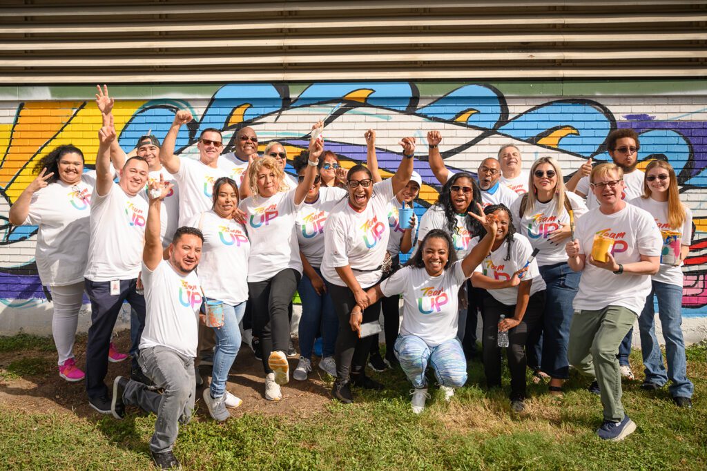 A large group of Team Up volunteers posing for a picture in front of mural