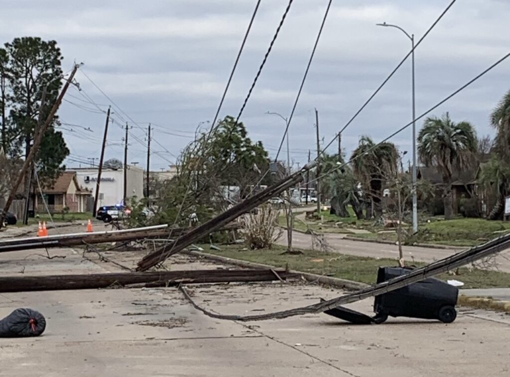 Power lines tangles in trees with debris and poles in street