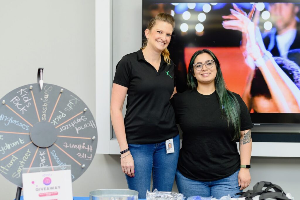 Two women wearing black Xfinity t-shirts posing behind a prize table.
