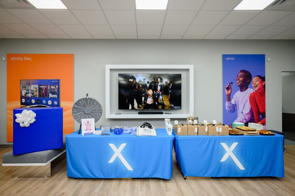 Two tables draped with blue tablecloth with Xfinity logo.