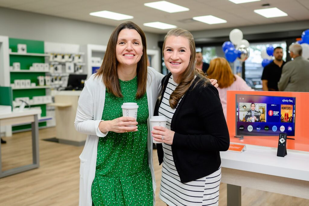 Two women holding coffee cups and smiling to post for a picture together.