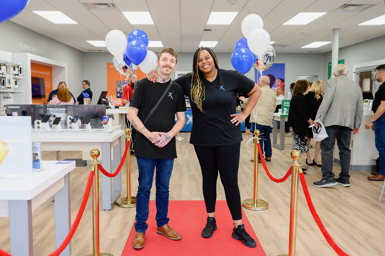 Two people wearing black Xfinity t-shirts standing at end of red carpet in Xfinity store