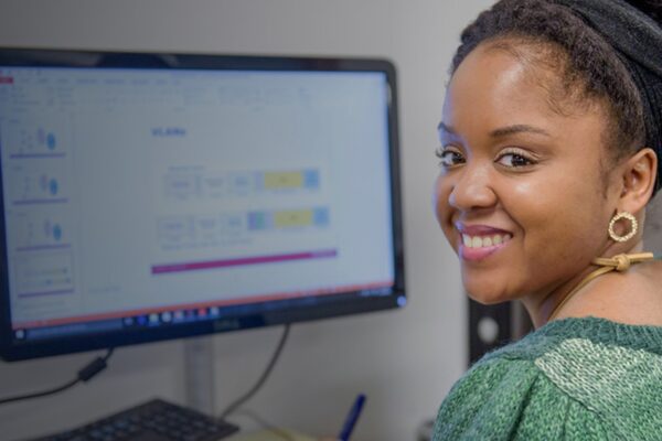 Smiling woman looking over her shoulder while sitting in front of desktop computer.