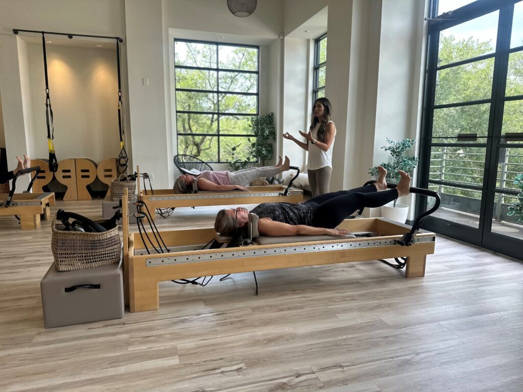 Two women laying on pilates tables receiving instruction