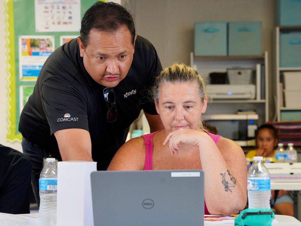 An instructor leaning to show a woman information on a laptop.