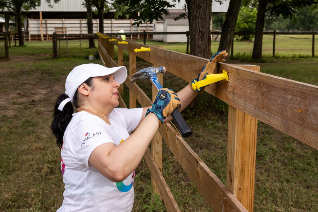 Team Up volunteer wearing white hat repairing fence with hammer