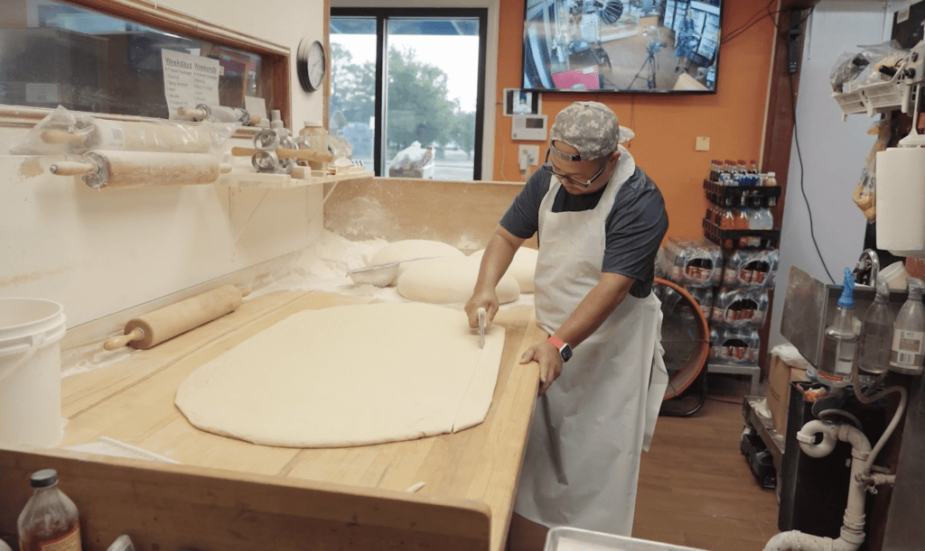Baker working on large amount of dough on a wooden workstation