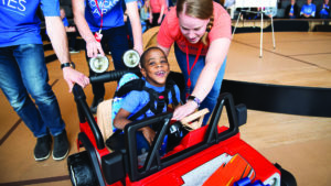 Easterseals volunteers help a young boy drive a toy car.