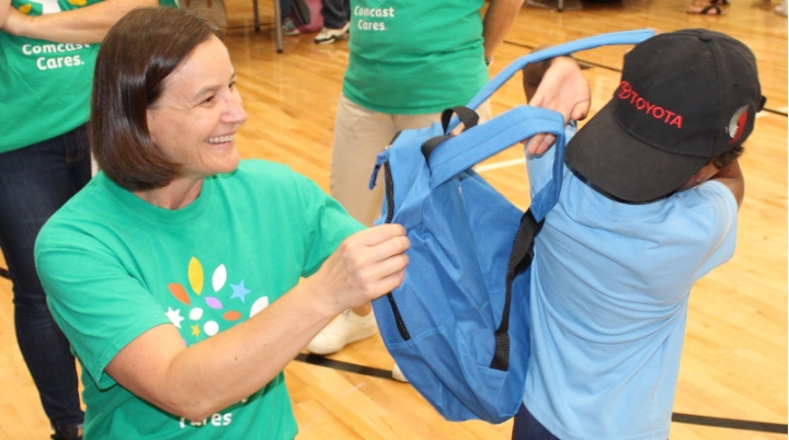 A Comcast Cares Day volunteer presents a child with a backpack.