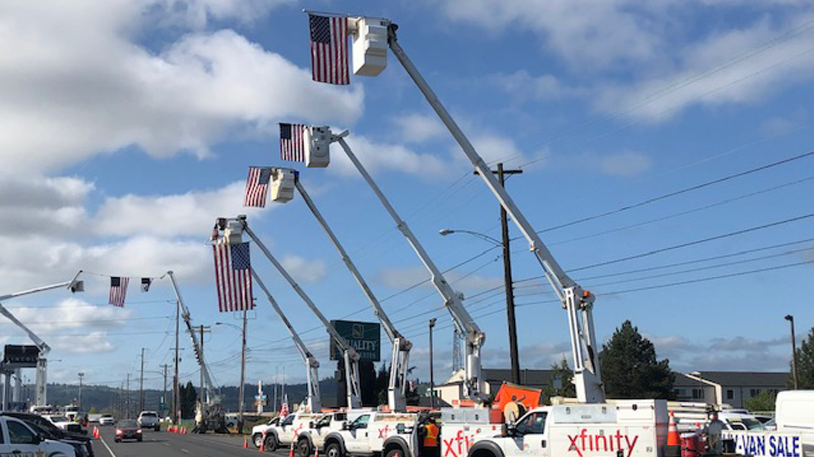 A series of Xfinity trucks with their cranes extended. Hanging from each crane is an American flag,